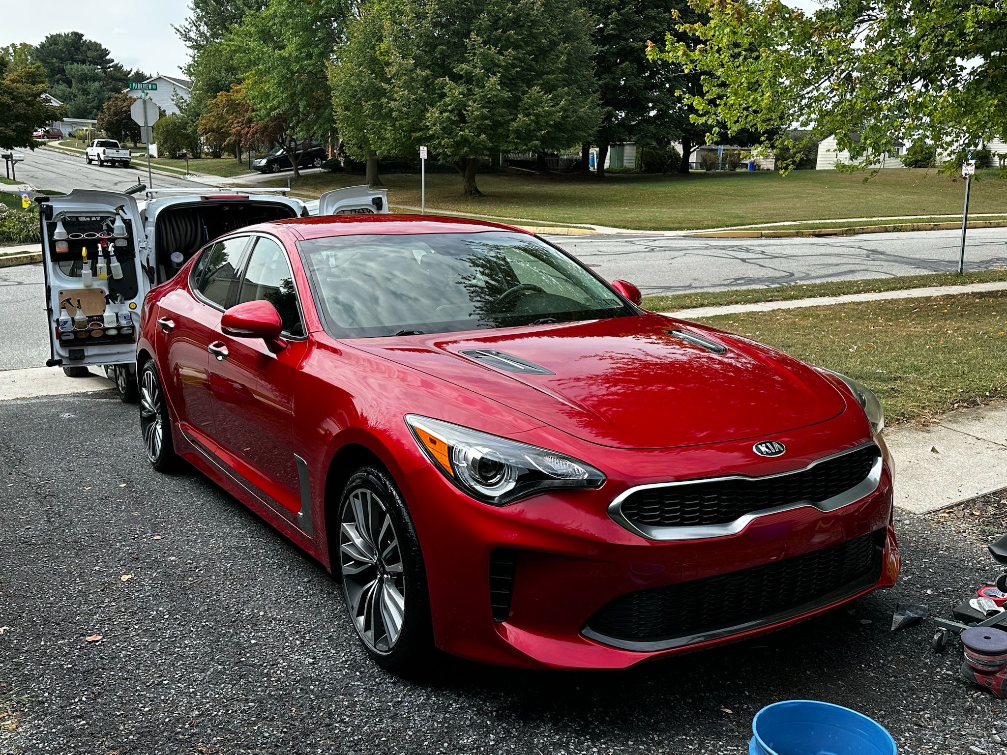 Red Kia sedan during mobile ceramic coating in York, PA, with detailing products on a service van nearby